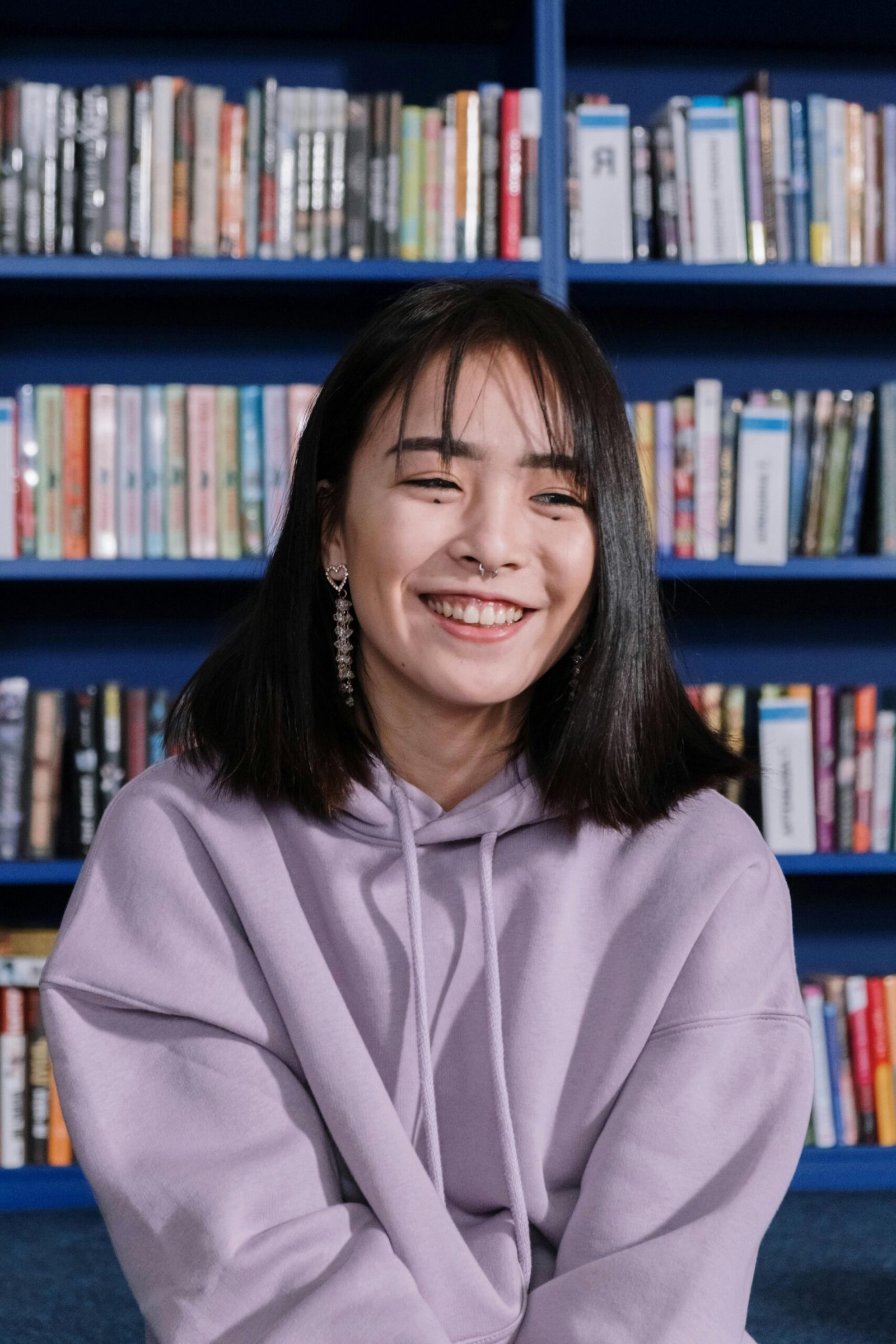 Happy teen girl in a purple hoodie sitting in a library with books in the background.